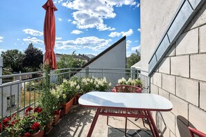 Ein Balkon mit Tisch, Stühlen, Blumentöpfen und einem roten Sonnenschirm.