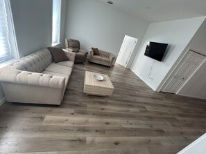 A living room with a sectional sofa, two armchairs, a coffee table, and a flat-screen TV mounted on the wall.