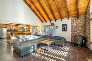 A spacious living room with a large gray sectional sofa, a wooden coffee table, and a stone fireplace.