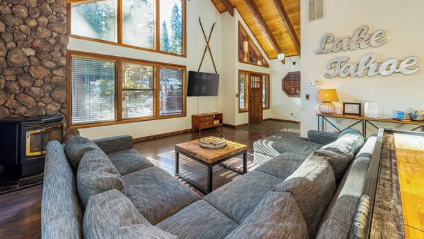 Amplia sala de estar con pared de piedra, ventanas grandes, chimenea y un letrero que dice "Lake Tahoe".