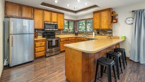 Una cocina moderna con armarios de madera, electrodomésticos de acero inoxidable, una isla grande con taburetes de bar y vistas al exterior a través de amplias ventanas.