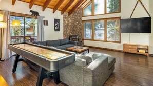 Un salón amplio con mesa de billar, asientos cómodos, ventanas grandes y una pared de piedra.