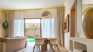 Ein modernes Wohnzimmer mit Steinwand, Flachbildfernseher, beiges Sofa, Holzesstisch mit Stühlen und einer großen abstrakten Skulptur.