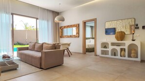 Ein modernes Wohnzimmer mit einer Couch, einem Glastisch und einer weißen Konsolentisch mit Dekoration. Ein großes Fenster mit Vorhängen, eine Deckenleuchte und Blick auf einen Pool im Freien.