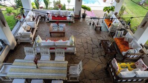 A covered outdoor seating area with stone flooring, white and wooden furniture, and potted plants. - RIZIKI YANGU HOUSE-4 BEDROOM LUXURIOUS HOUSE (Malindi)