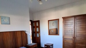 Una camera da letto con testiera in legno, un letto con copripiumino a fiori blu, un armadio in legno, un piccolo tavolino e uno specchio appeso al muro.