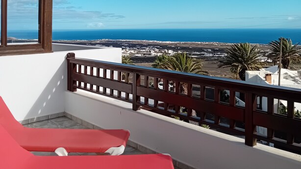 Un balcone con poltrone rosse, ringhiera in legno e vista sul mare e sugli edifici.