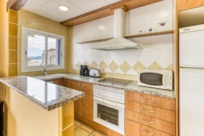 Une cuisine avec une fenêtre, une cuisinière, un four à micro-ondes et des armoires en bois.