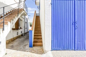 Une ruelle étroite avec un escalier en bois menant à un immeuble, une porte bleue et un sol pavé de pierres.