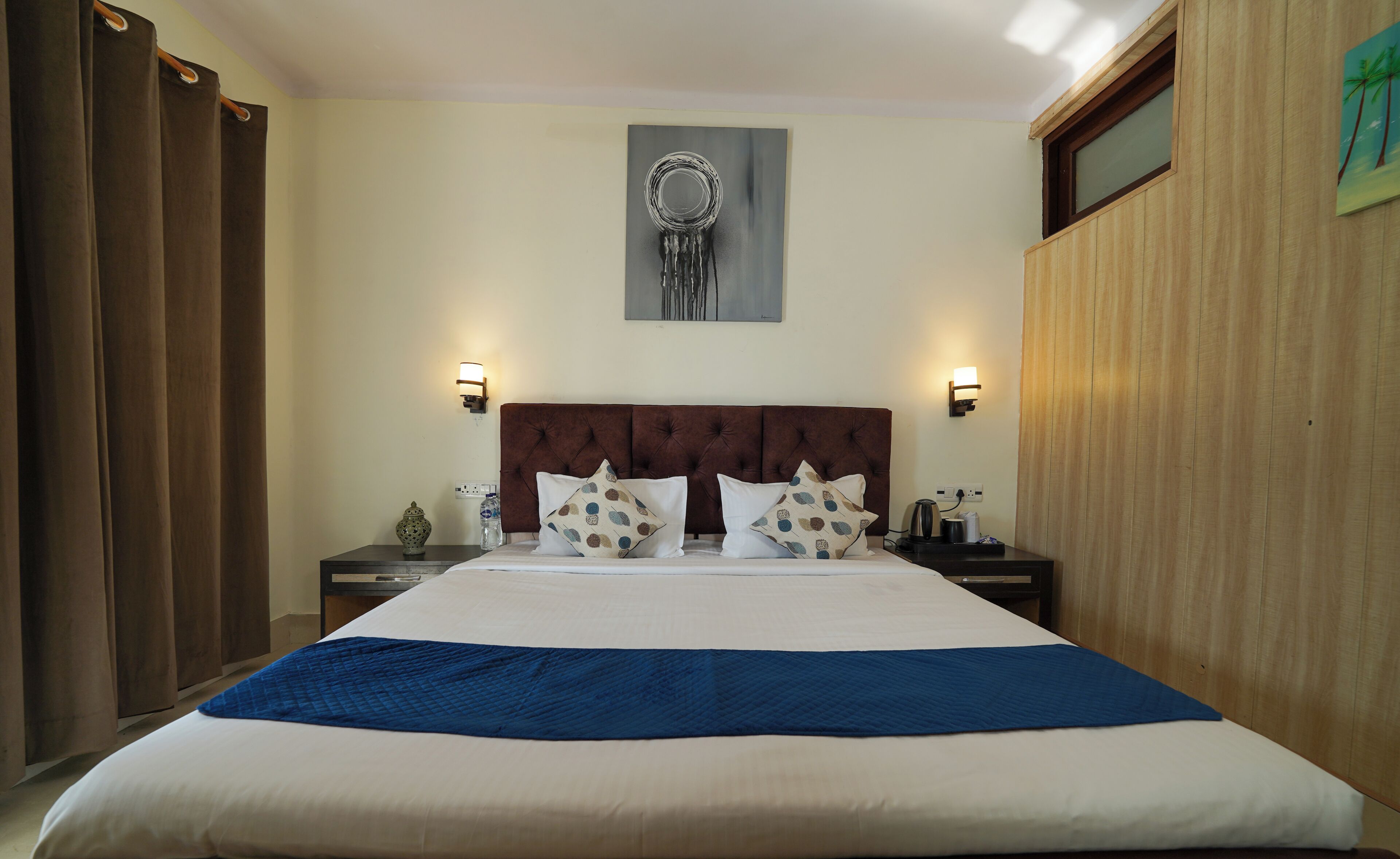 A hotel room with a large bed, two bedside tables, a wall-mounted artwork, and a window with a view.