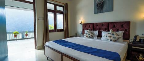 A bedroom with a large bed, a view through an open door, a bedside table with a lamp, and a wall-mounted artwork.