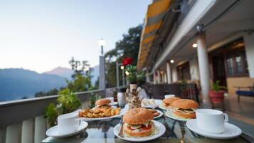 Una mesa de comedor con comida y bebidas en una terraza con vista a la montaña.