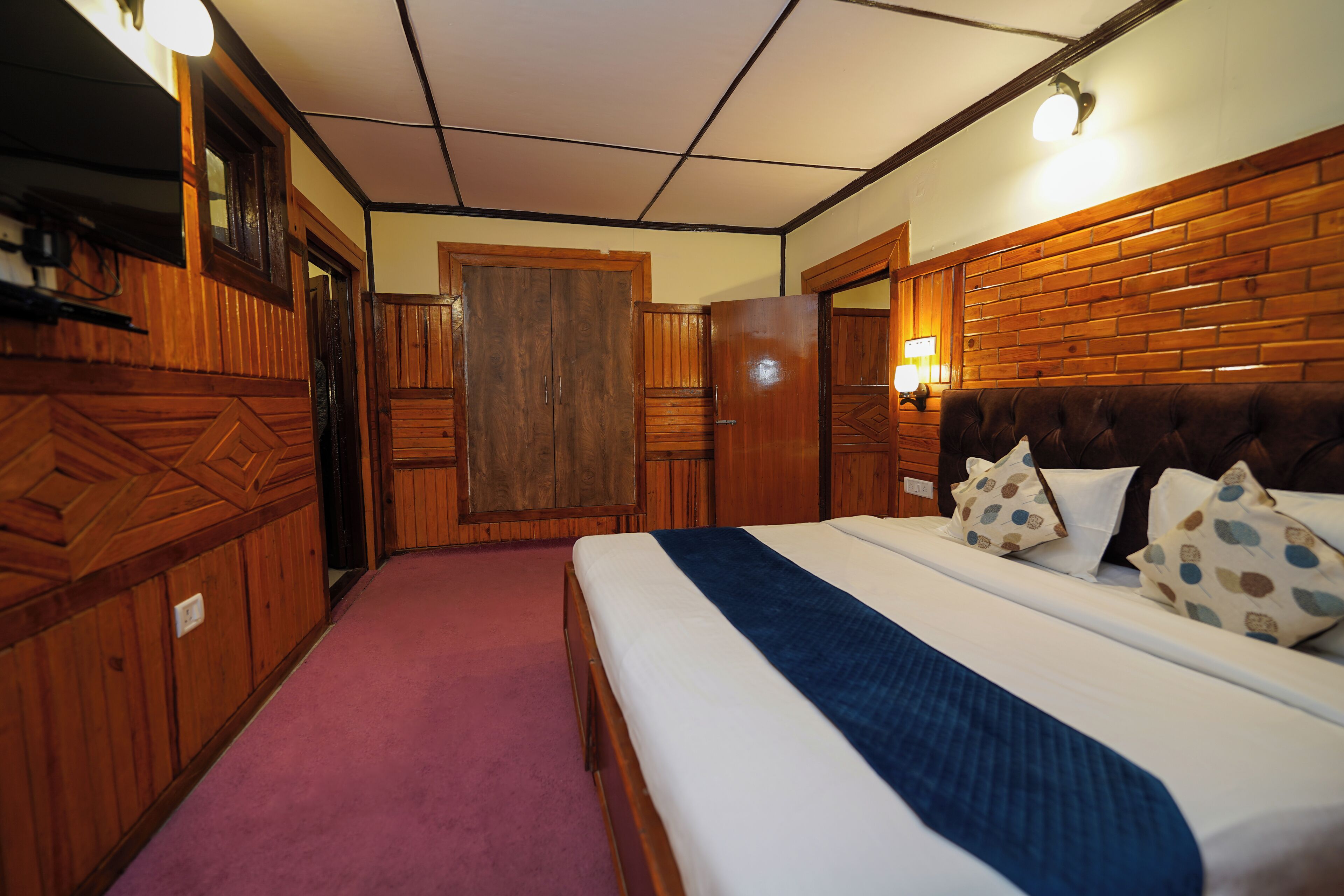Habitación de hotel con cama, paneles de madera, una puerta y un aplique.