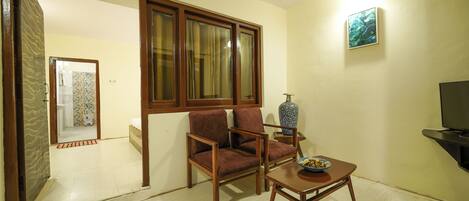Una sala de estar con sofá, mesa de centro, televisor y ventana con cortinas.