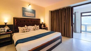 A hotel room with a large bed, a headboard, bedside tables, a nightstand, a window with curtains, and a view of the outside. -  Hotel Silverton (180 lake view)  (Nainital)