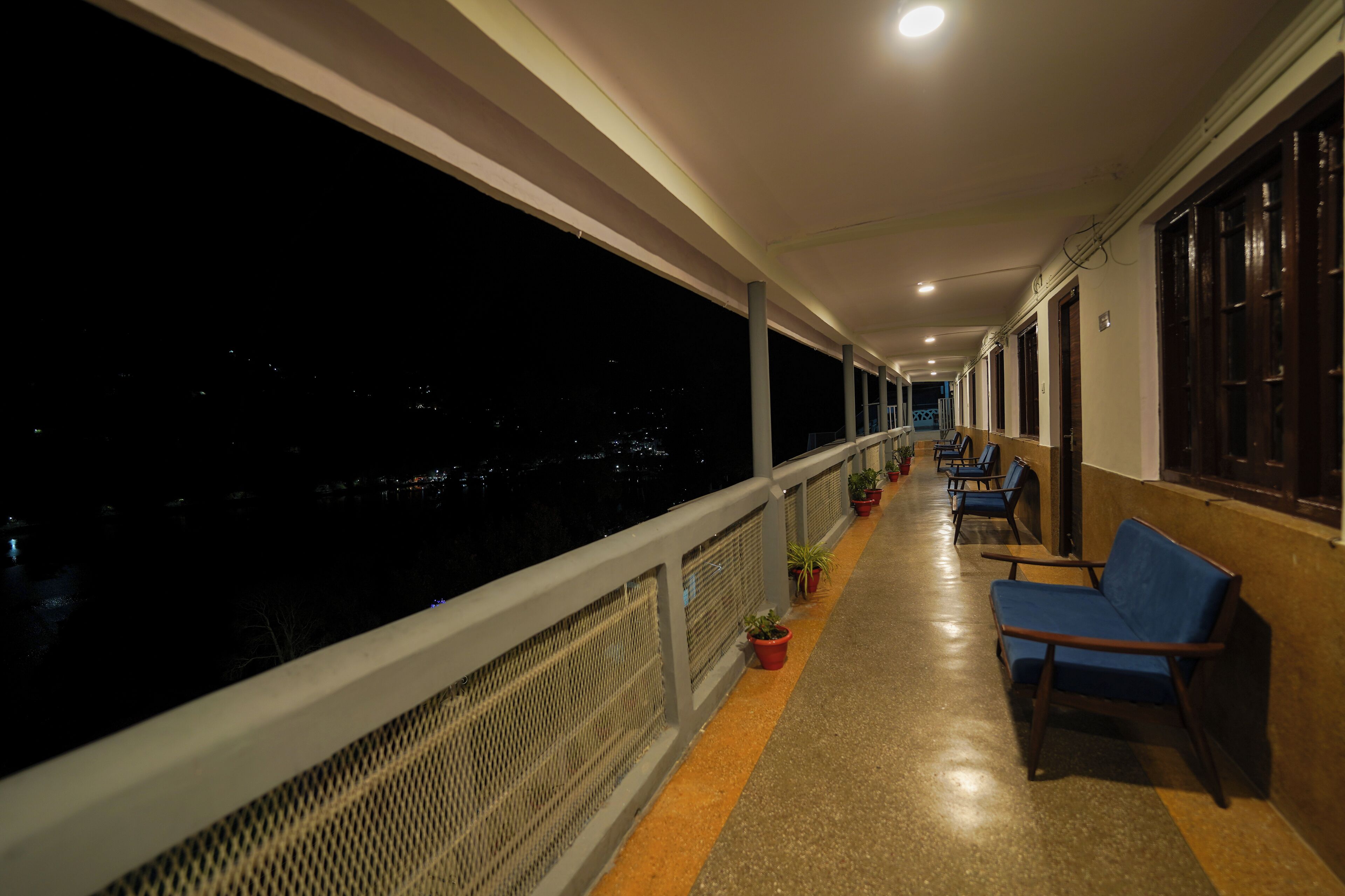 A corridor with a railing, potted plants, and blue chairs.