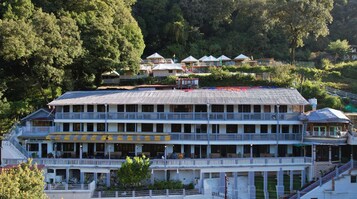 Et hotel med flere etager, altaner, en swimmingpool og udsigt til den omkringliggende skov.