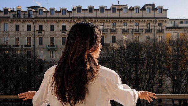 Una persona de pie con los brazos extendidos, observando una hilera de edificios con varios pisos y balcones.