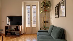 Una sala de estar con sofá, televisor, estantería y puerta que da a un balcón exterior.