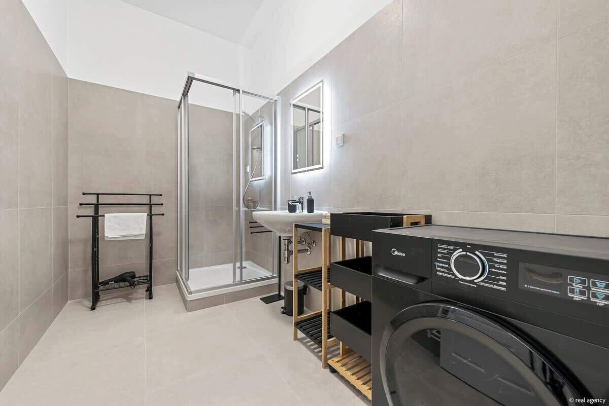 Une salle de bain moderne avec une douche à parois de verre, un lavabo, un lave-linge noir et un porte-serviettes.