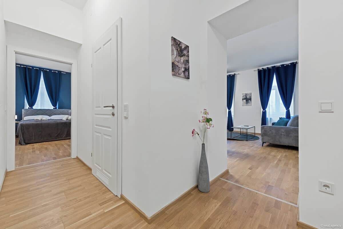 Eine moderne Wohnung mit Holzboden, einer weißen Tür, einer Vase mit Blumen und einem grauen Sofa.