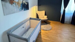 Una sala de estar moderna con una cuna para bebé, un cuadro abstracto grande, una silla y una lámpara de pie.