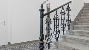 Una escalera con barandillas negras ornamentales y un pasamanos, que lleva a un rellano con una puerta.