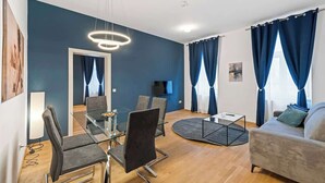 Una sala moderna con una mesa de comedor de vidrio, sillas grises, un sofá y un televisor.