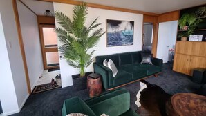 Ein modernes Wohnzimmer mit einem grünen Sofa, einer großen Topfpflanze und einem Gemälde einer Welle.
