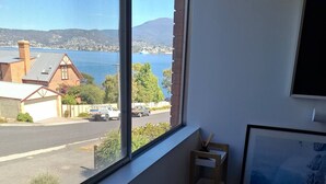 Ein Zimmer mit großem Fenster und Blick auf eine Straße, Gebäude und ein Gewässer.