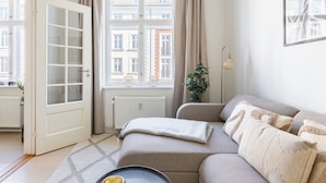 A living room with a sofa, a radiator, a window with curtains, a door, and a plant. - Shield 2 - Great Apartment in the Centre of Copenhagen (Copenhagen)