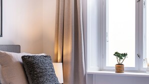 A bed with pillows, a bedside lamp, a window with a plant, and a view of the sky. - Shield 2 - Great Apartment in the Centre of Copenhagen (Copenhagen)