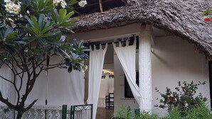 Una cabaña con techo de paja, cortinas blancas, un portón y un camino que conduce a una habitación interior.