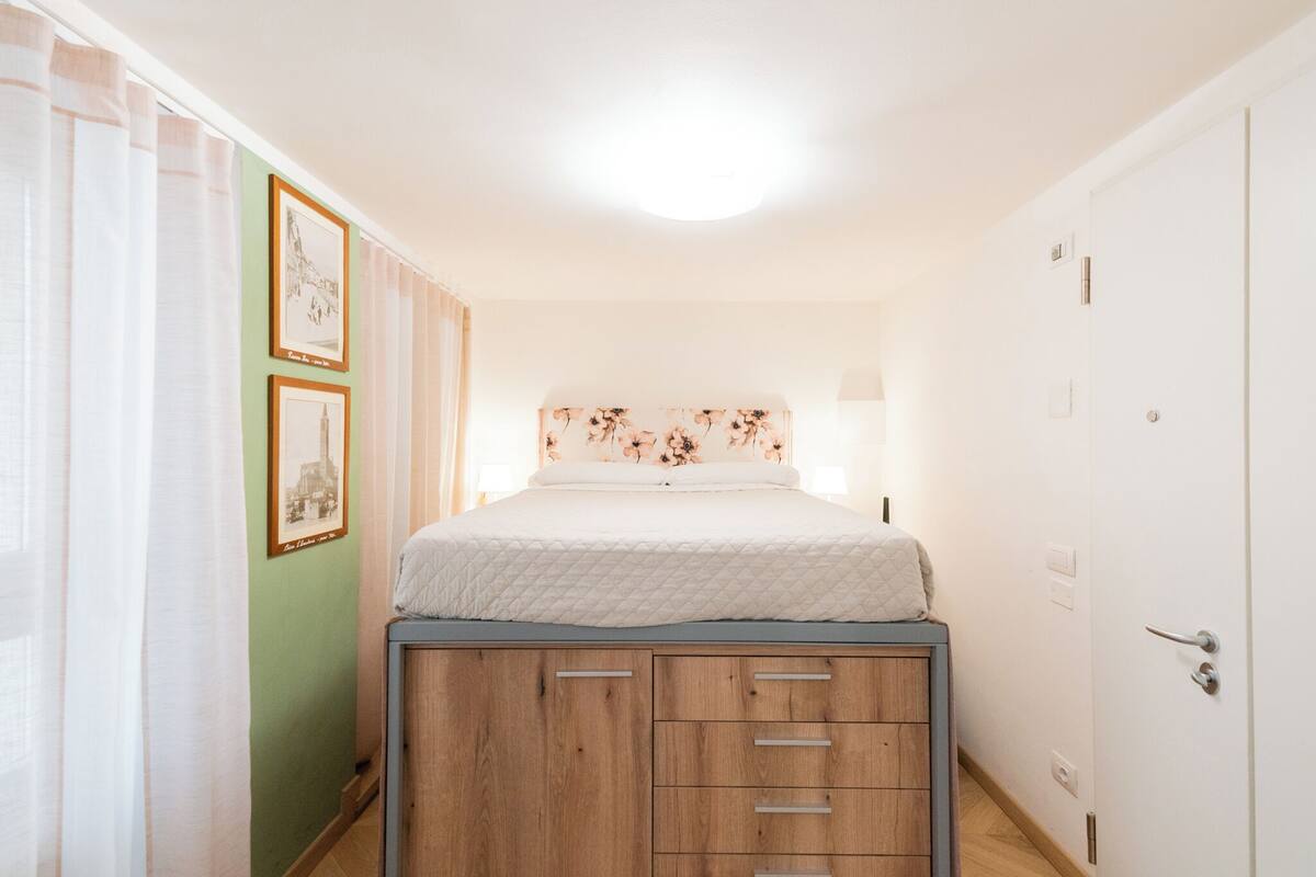 Un dormitorio con cama, cómoda de madera, mesita de noche y luz empotrada.