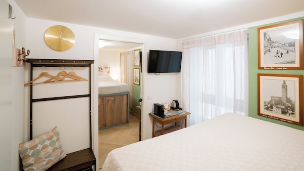A hotel room with a bed, a desk with a computer, a TV, a clock, and a coat rack. - Cozy room in the heart of city (Verona)