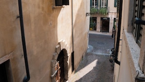 A narrow cobblestone street between buildings with a shop on the right and a closed shutter on the left. - Cozy room in the heart of city (Verona)