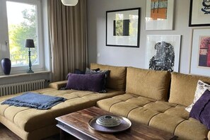 A living room with a sofa set, a coffee table, and a window with curtains. - Sunshine | Seenah | seeglueck (Konstanz)
