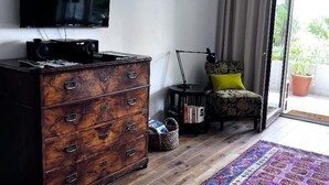 Un salón con un aparador de madera, un televisor, un sillón estampado y vistas a través de una puerta de cristal.