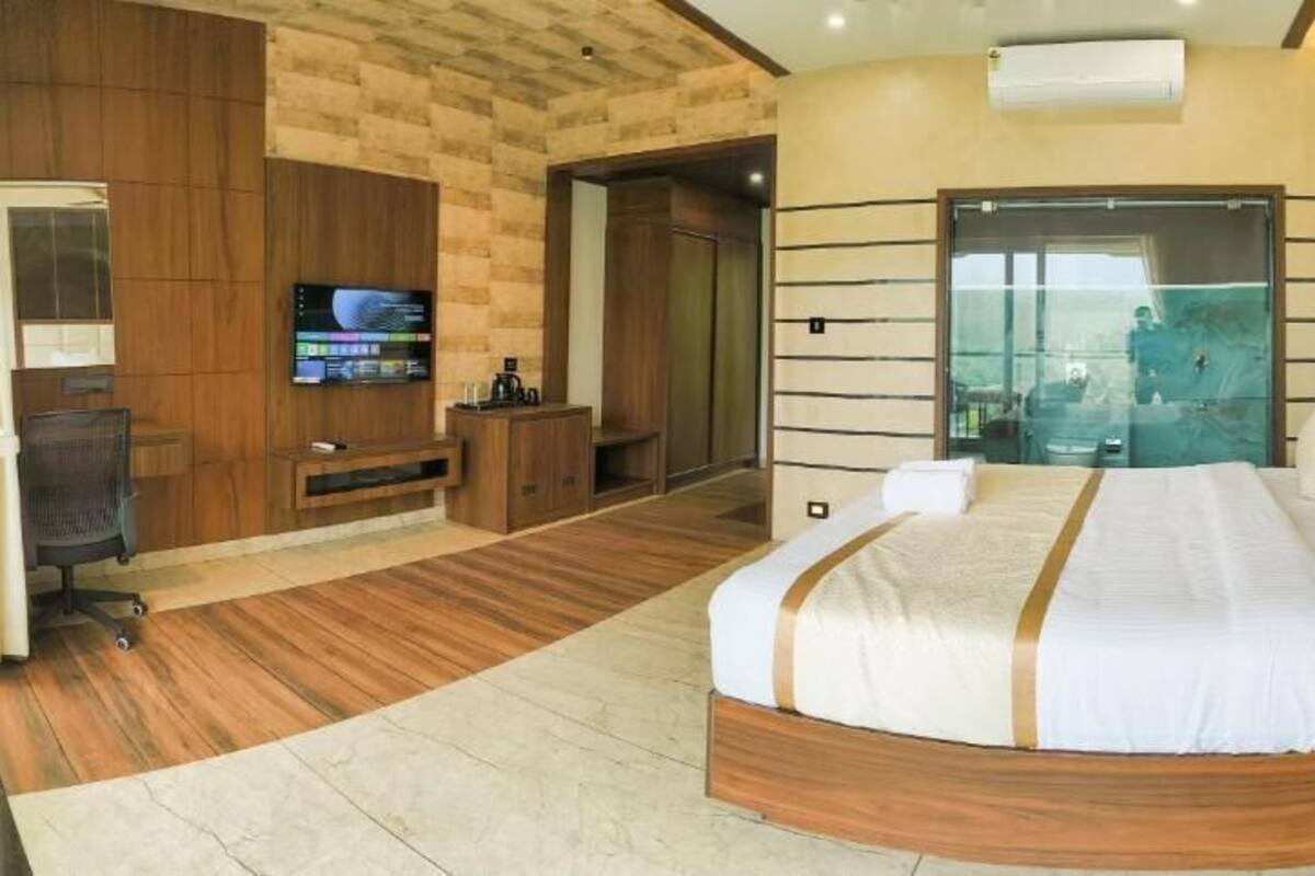 Une chambre moderne avec un grand lit, une télévision, un bureau et une porte-fenêtre coulissante donnant sur un balcon.