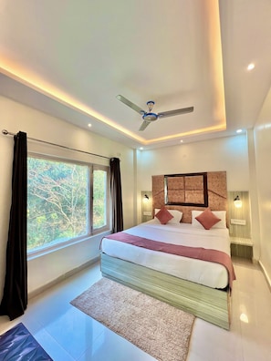 A modern bedroom with a large bed, ceiling fan, and a window with curtains. - The White Rain Hotel (Lansdowne)