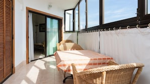 En balkon med et bord og stole, en skydedør og udsigt til himlen.