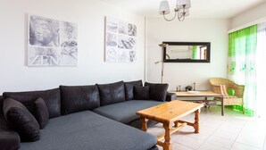 En moderne stue med en grå hjørnesofa, et træsofabord og en grøn lænestol. To billedrammer og et spejl hænger på væggen over et lille bord.