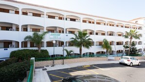 Et hotel med flere etager, altaner, palmer og en parkeringsplads.