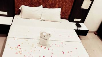 Una cama bien hecha con sábanas blancas, una toalla decorativa y pétalos de rosa esparcidos.