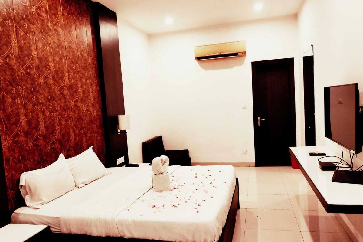 A hotel room with a large bed, a TV, a desk, and a door.