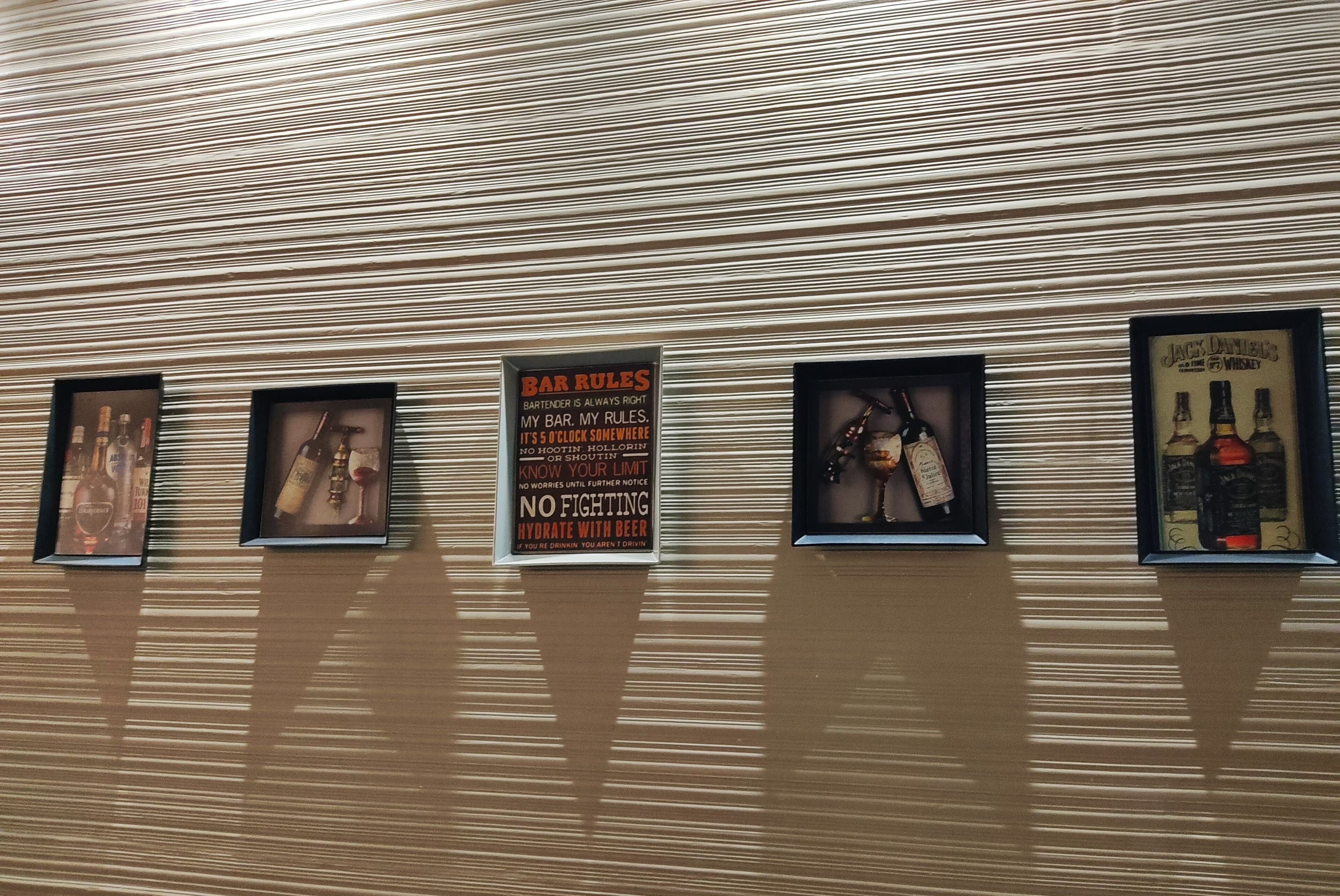 Una pared con elementos decorativos, incluyendo un cartel con las normas del bar y botellas de licor enmarcadas.