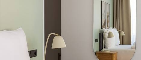 A hotel room with a bed, a bedside lamp, a nightstand, a mirror, and a door leading to another room.