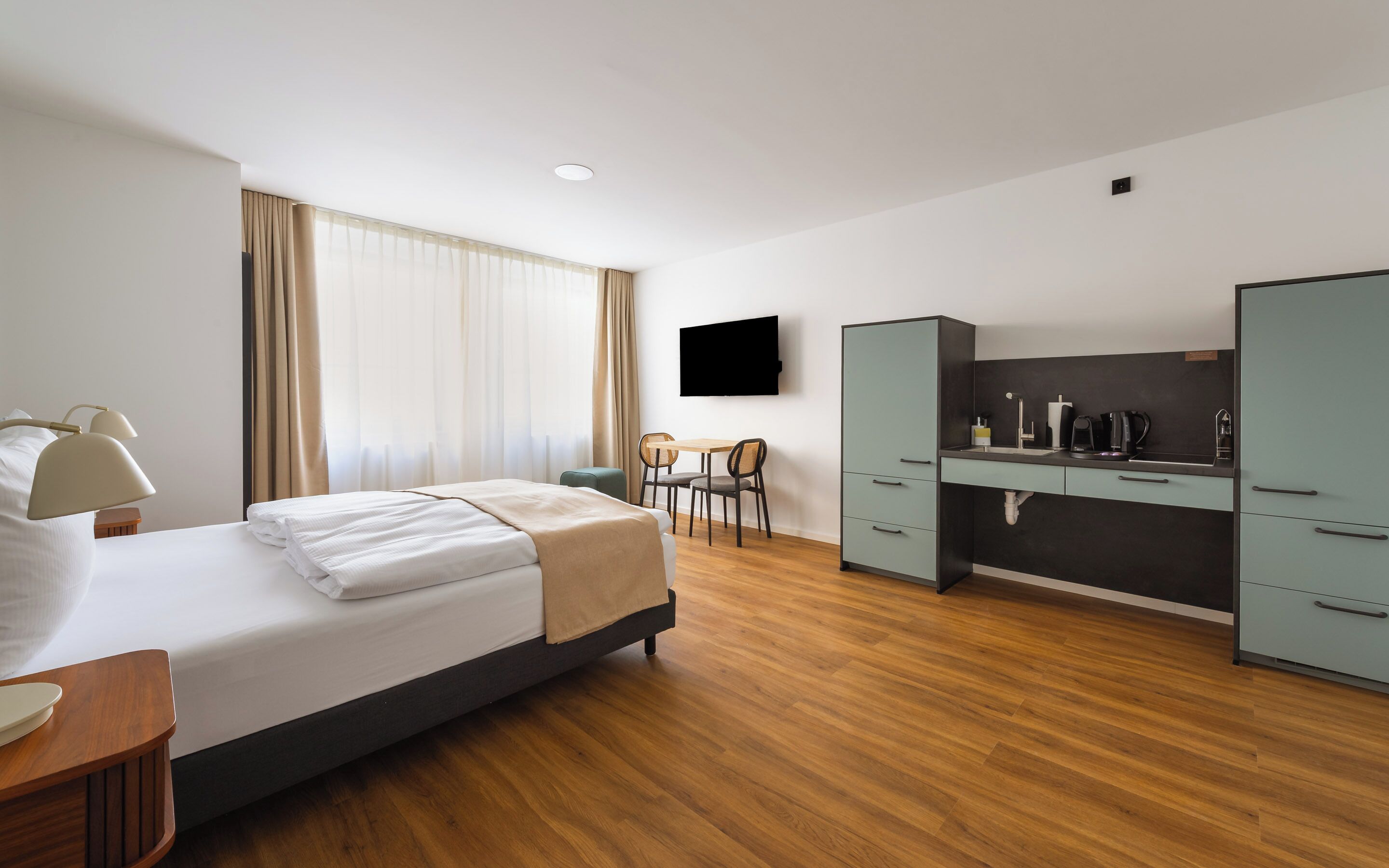 Ein Hotelzimmer mit Bett, Schreibtisch mit Stuhl, Fernseher und einer Küchenzeile.