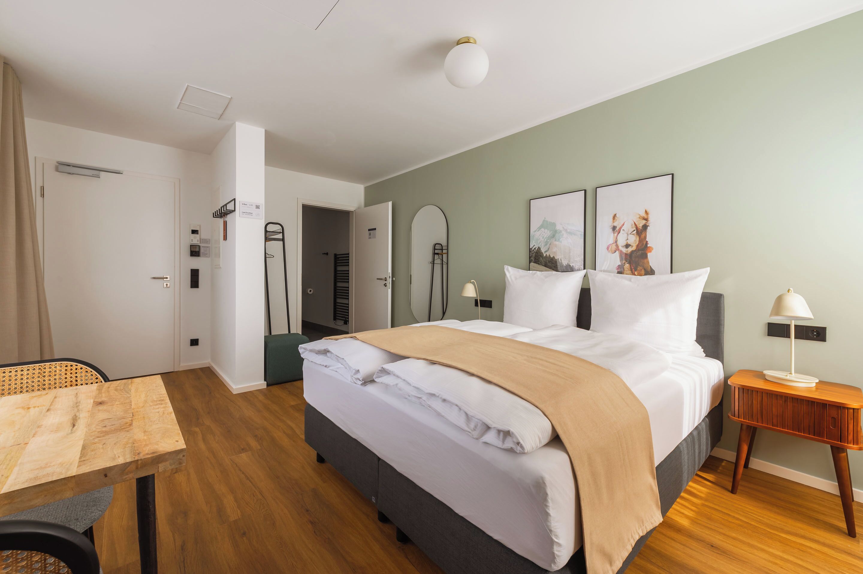 Habitación de hotel con cama, mesita de noche, lámpara y vista al baño.