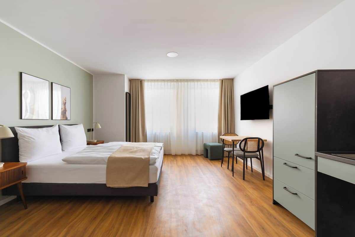 A hotel room with a bed, bedside tables, a desk with a chair, a wardrobe, and a TV mounted on the wall.